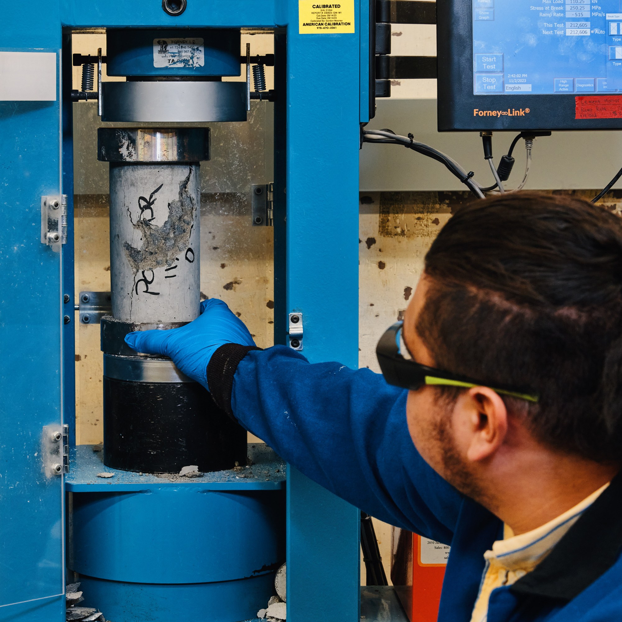 a worker reaches into a machine to grab a cylinder of cement