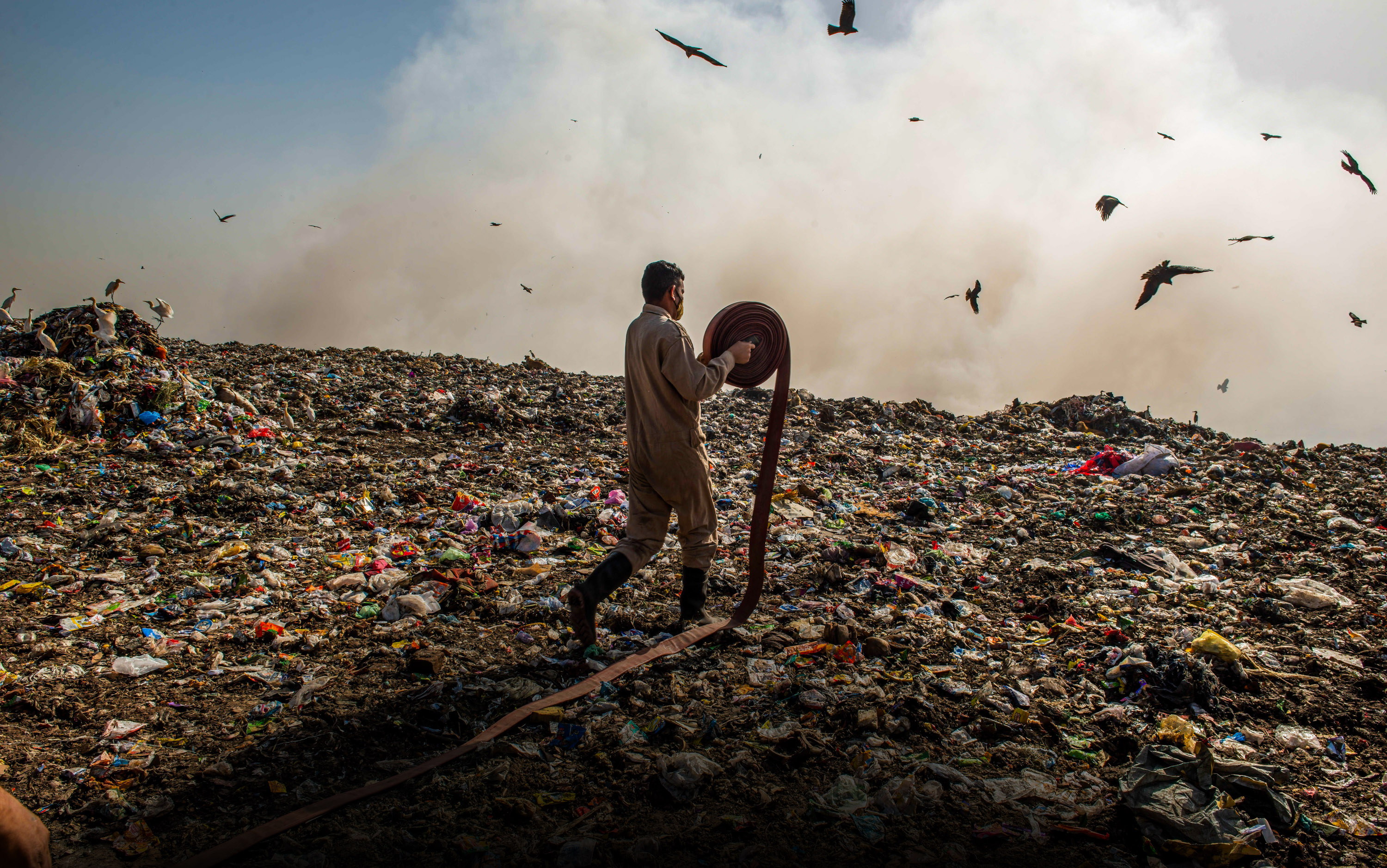 A Delhi Firefighter laying pipe trying to control fire at Ghazipur landfill site