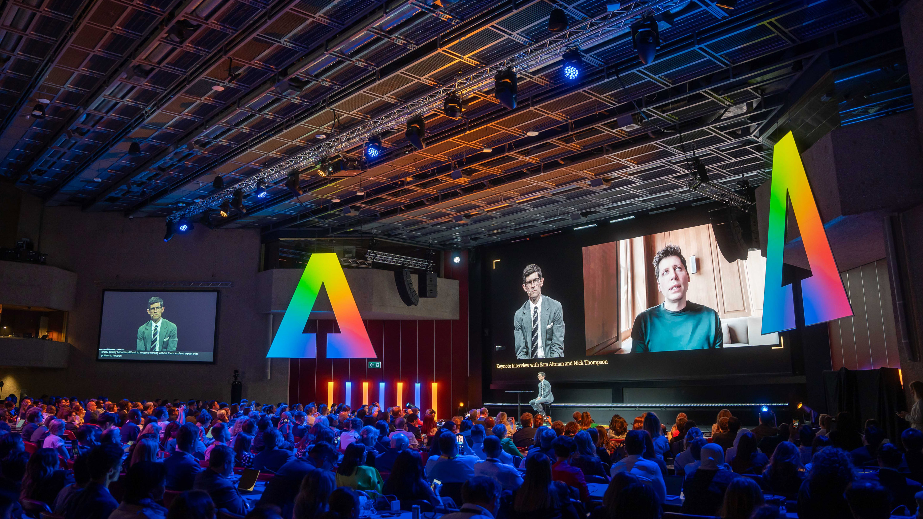 the crowd and stage at AI for Good event during the interview with Sam Altman (seen on screen) and Nick Thompson (live, and on-screen)