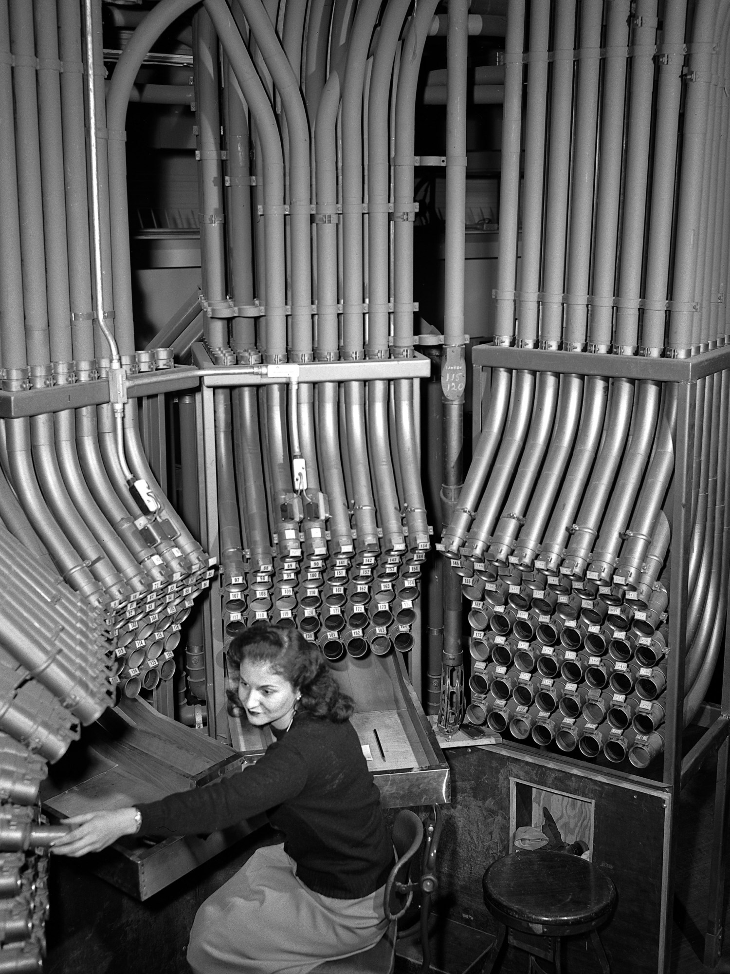 a woman stationed in front a mass of pneumatic tubes